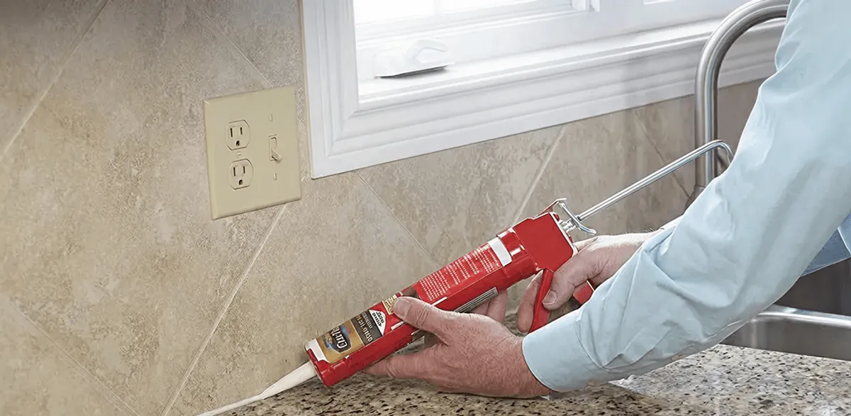 Handyman applying caulk along a kitchen backsplash and countertop seam in Fort Wayne, IN