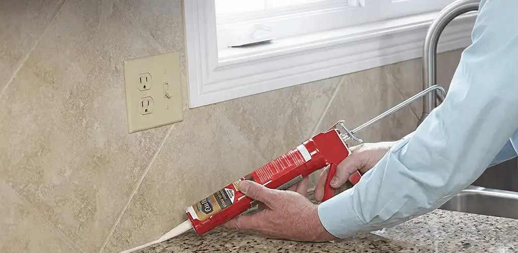 Handyman applying caulk along a kitchen backsplash and countertop seam in Fort Wayne, IN