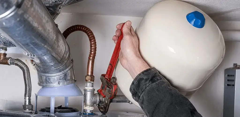 Water heater repair technician tightening plumbing connections near a tank unit in Fort Wayne, IN